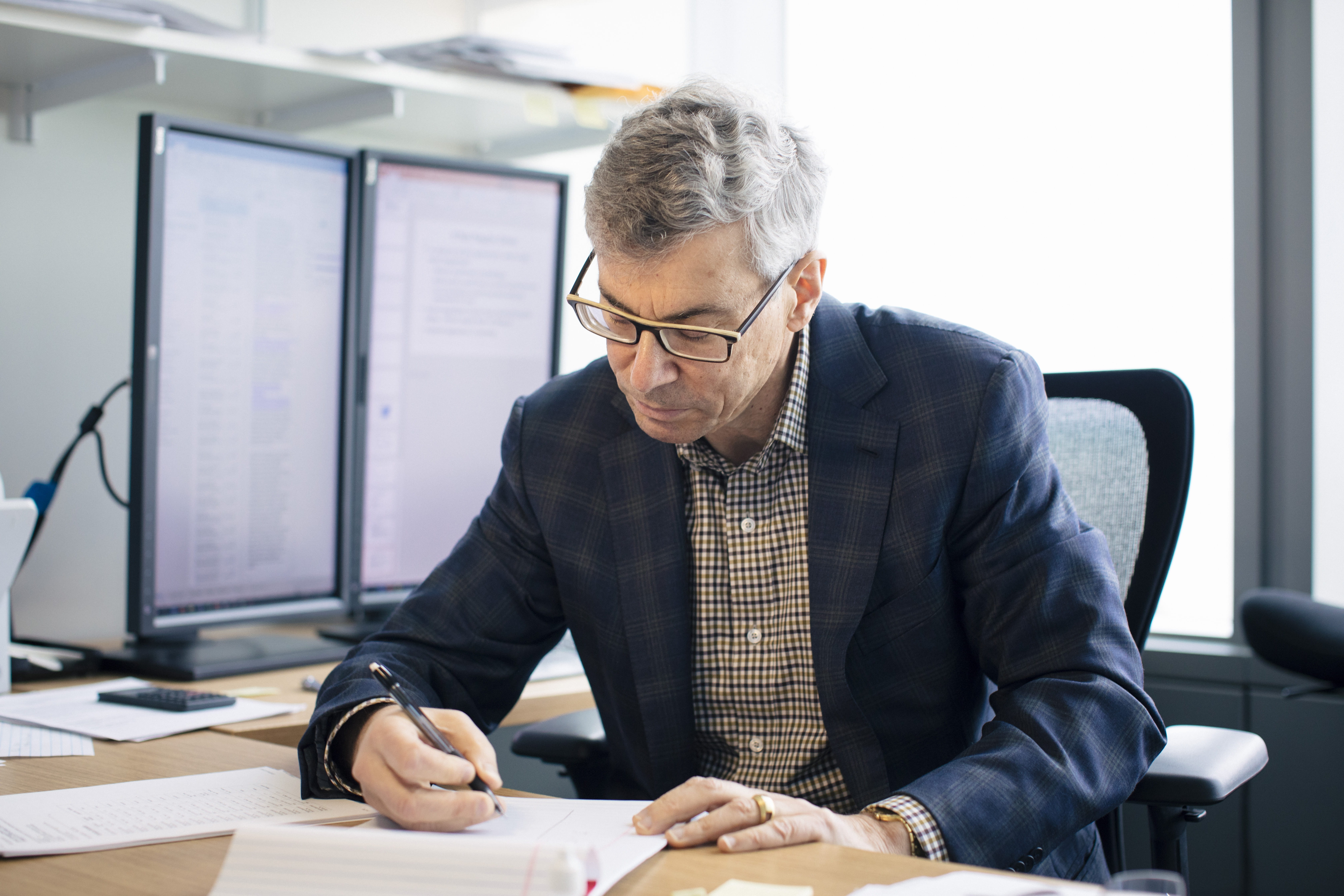 Professor David Dranove seated at a desk in the Kellogg Global Hub, writing in a legal pad.