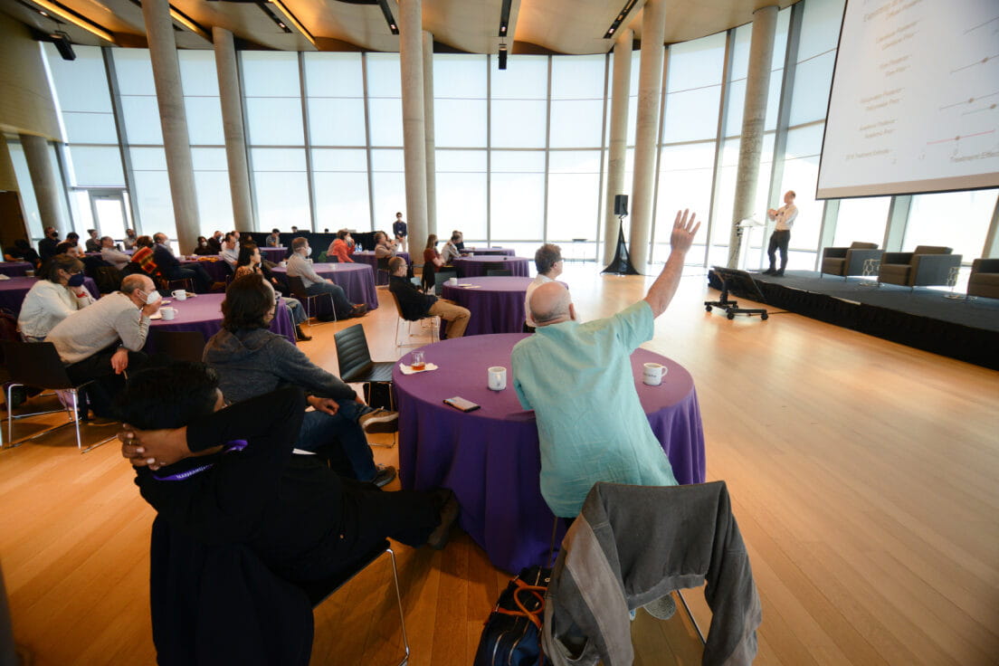 man raising his hand with people sitting around tables at a Global Poverty Research Lab event held in the Kellogg global hub