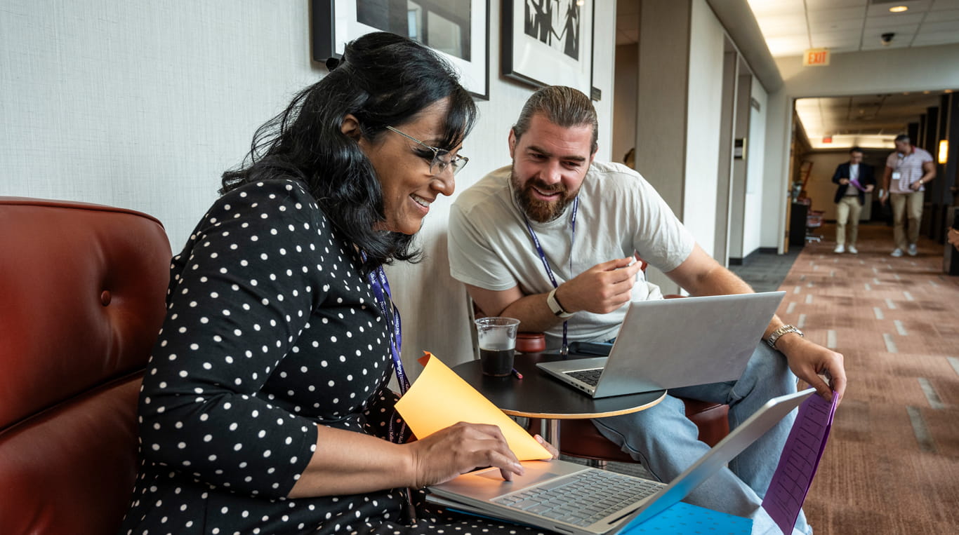 Two EMBA students share work on their laptops