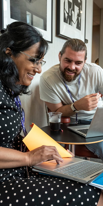 Two EMBA students share work on their laptops
