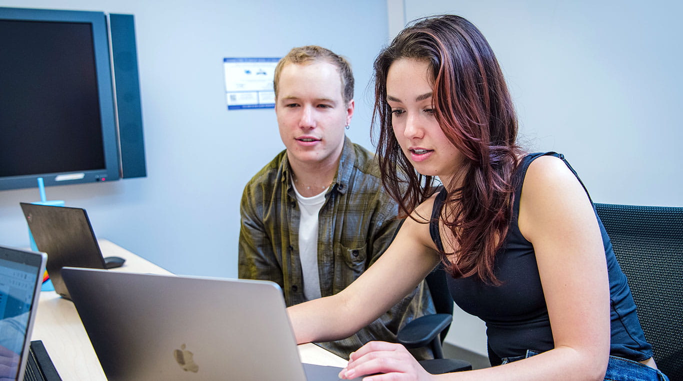 Two students sitting down looking at a laptop