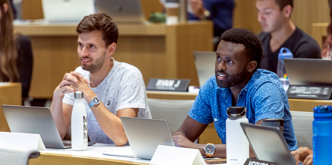 Two MBA students sitting with classmates during a professor's lecture.