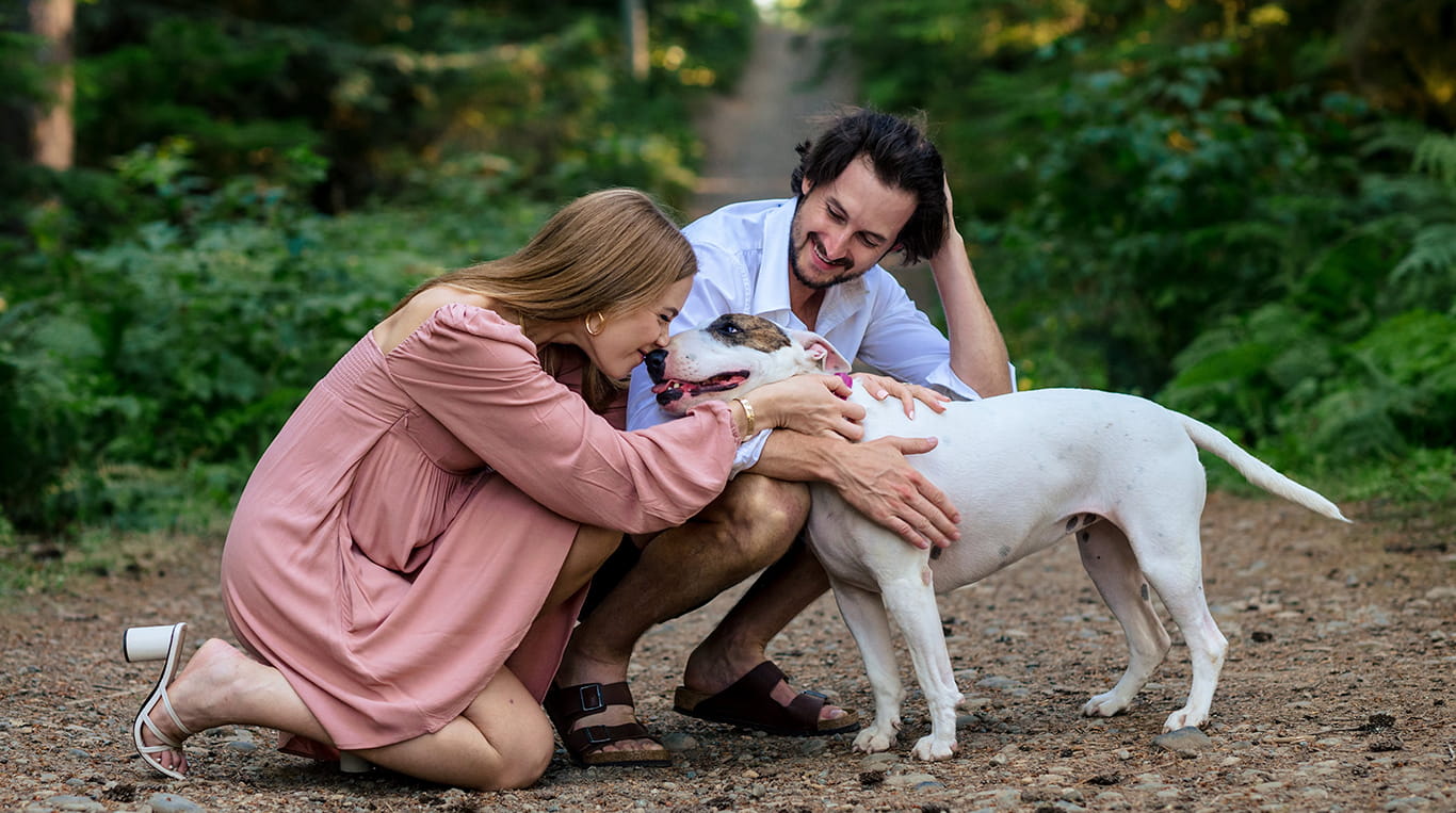 Kellogg student Alex Tyrell and her partner lean down to pet their dog, while out for a walk on a forest trail.
