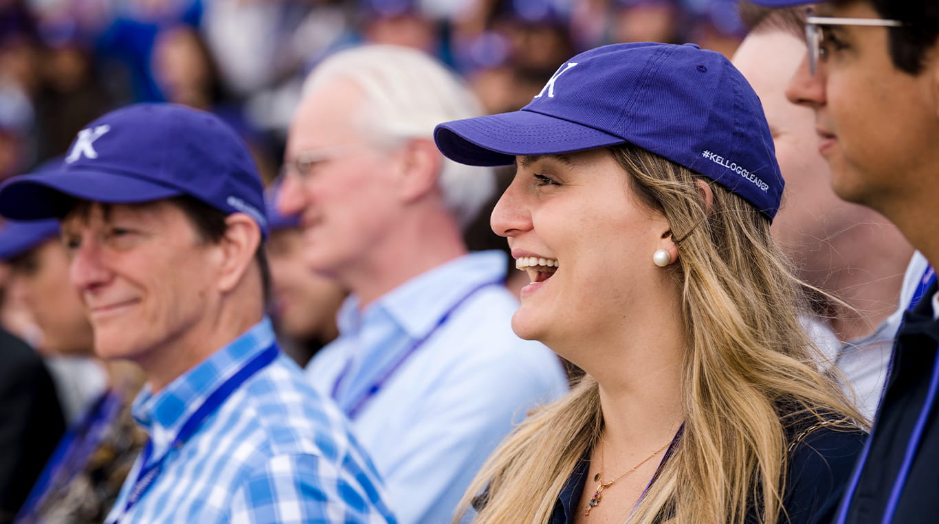 A Kellogg alumna with fellow graduates at reunion. She is wearing a purple baseball cap with the Kellogg logo on the front and #KelloggLeader on the side.