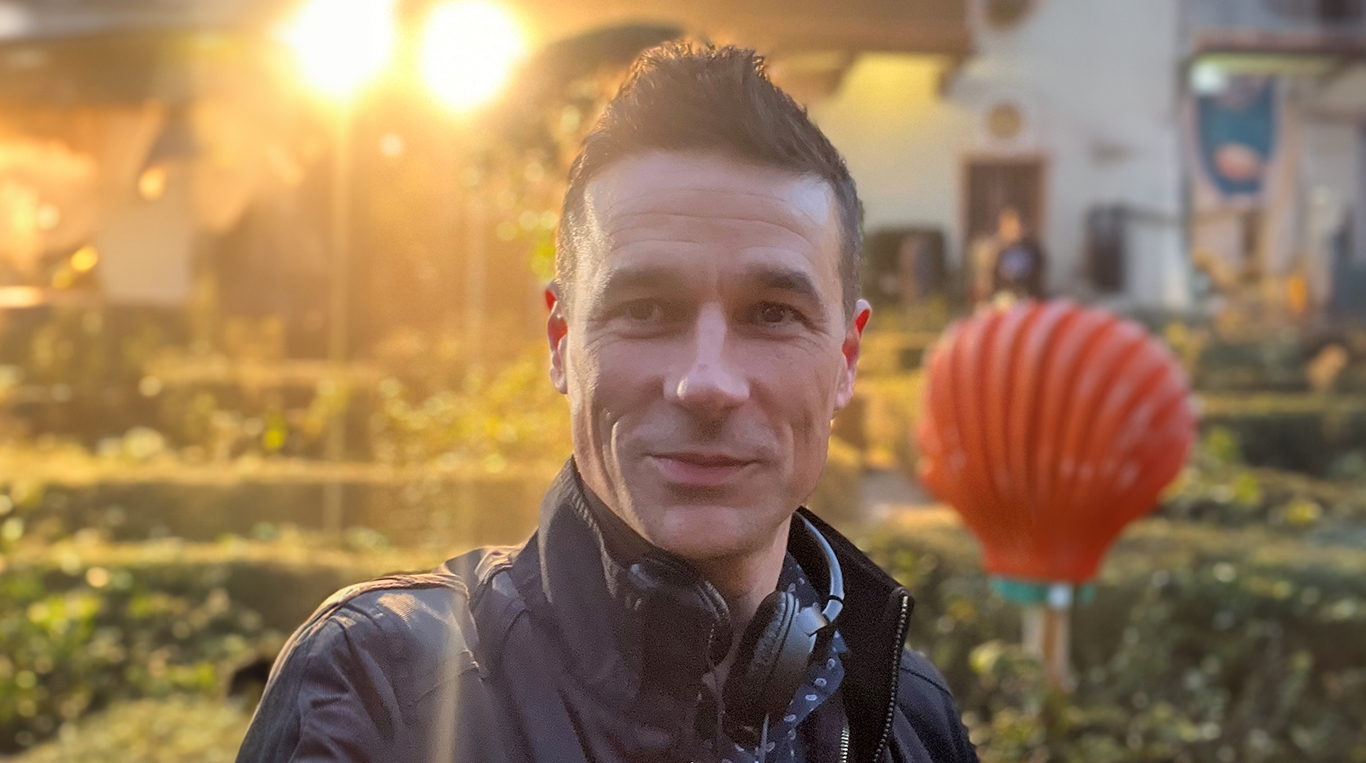 Kellogg alum Chris Brody stands outdoors near a garden while a warm light shines in the background