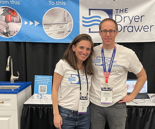 Kellogg alum Nic White-Petteruti and his wife Courtney Baron stand in front of the Dryer Drawer's booth at a trade show.
