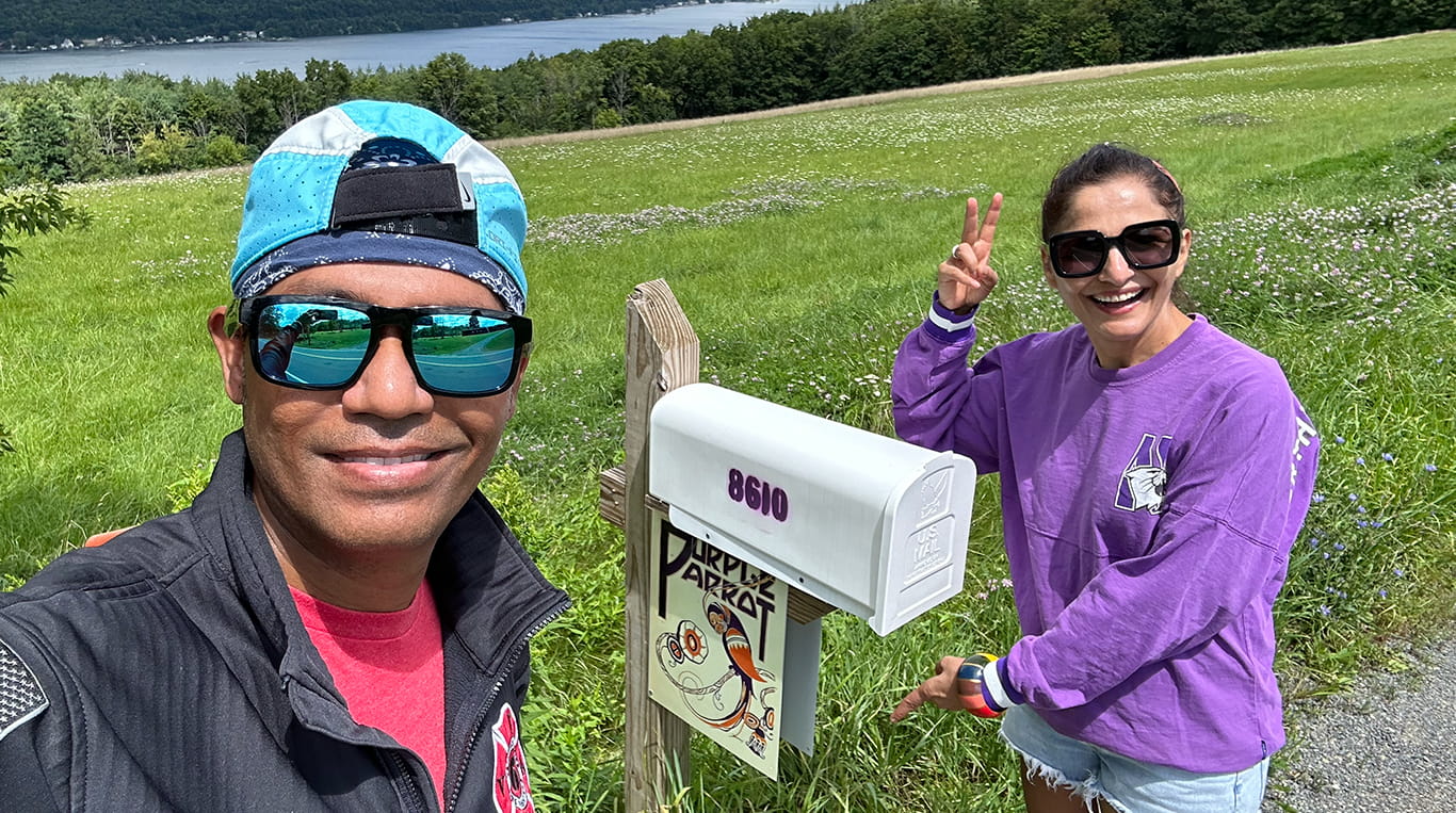 Kellogg alumni Satish Annadata and Indra Sandal stand outside next to a mailbox decorated with a sign reading "Purple Parrot." Indra wears a purple Northwestern sweatshirt.