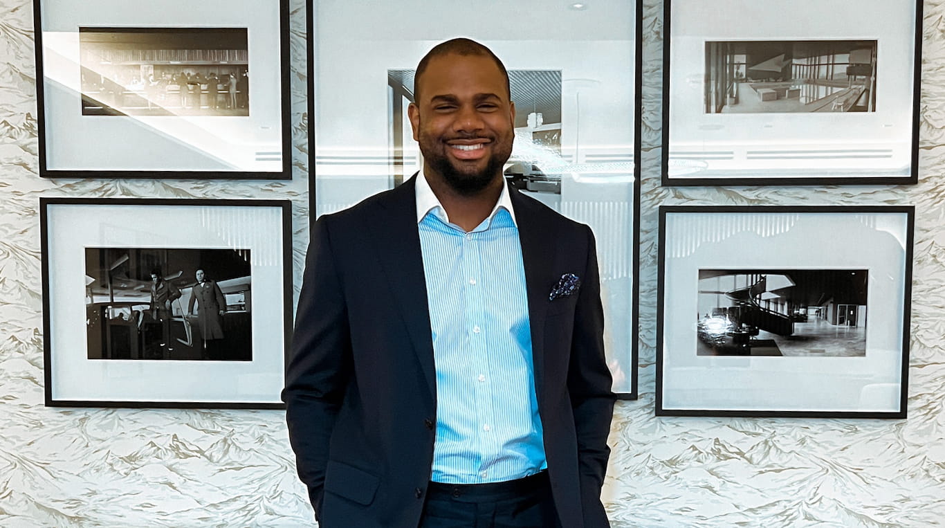 Evening & Weekend MBA student Reuben Aniekwu stands in front of a wall of framed photographs.