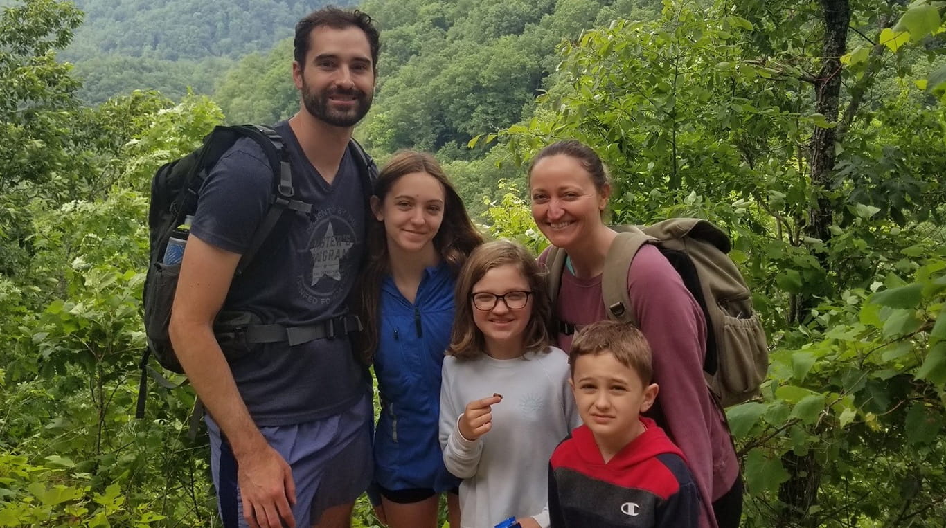 Kellogg graduate Gerry Sapienza '21 MBA poses with his wife and three kids while they are on an outdoor hike in a forest.