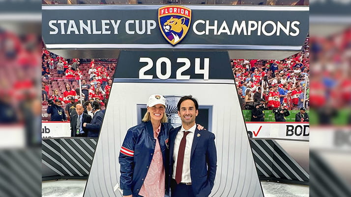 Mark Zarthar and his wife, Kathleen, pose at an ice rink near a sign reading "Stanley Cup Champions 2024"