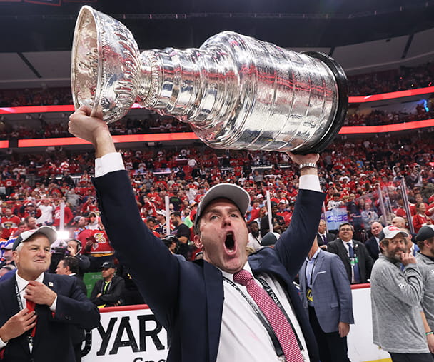 Matt Caldwell celebrates and holds the Stanley Cup over his head, celebrating on the ice after the NHL's Florida Panthers won the 2024 championship.