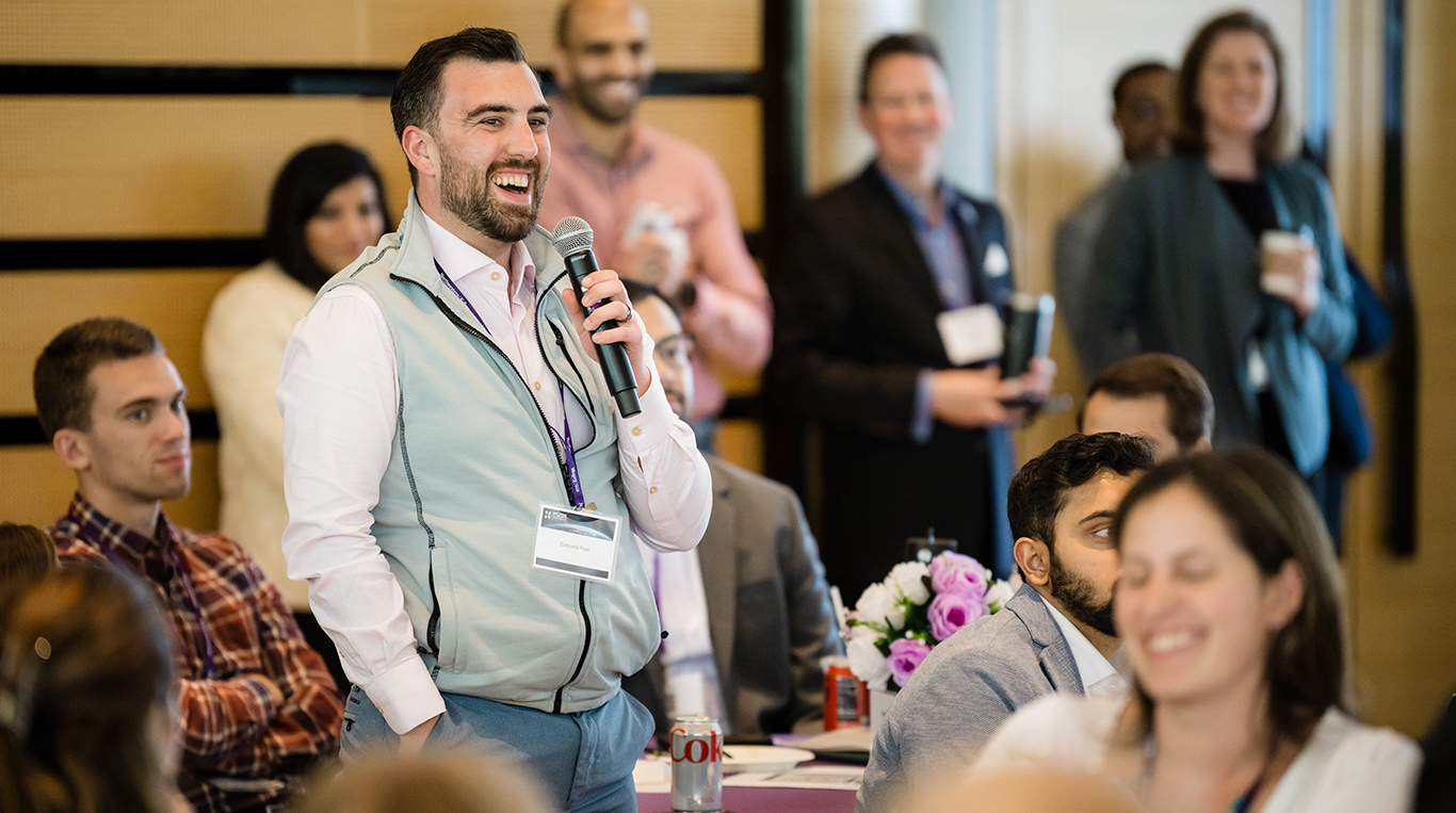 An attendee at Kellogg's student-run Climate Conference smiles while holding a microphone to ask a question.