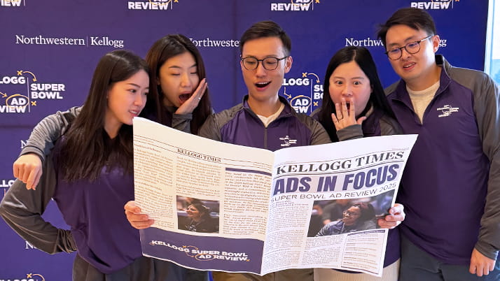Kellogg MBA students holding an oversized newspaper during Super Bowl Ad Review, an annual event that brings together MBA students to evaluate and rate Super Bowl ads in real-time.