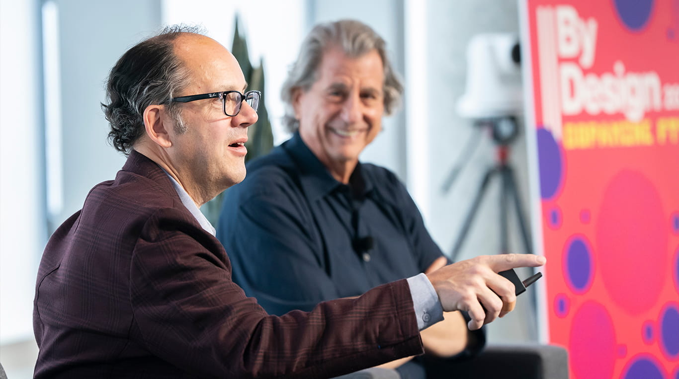 Two men on stage engaging talking with one another about the role design plays in business