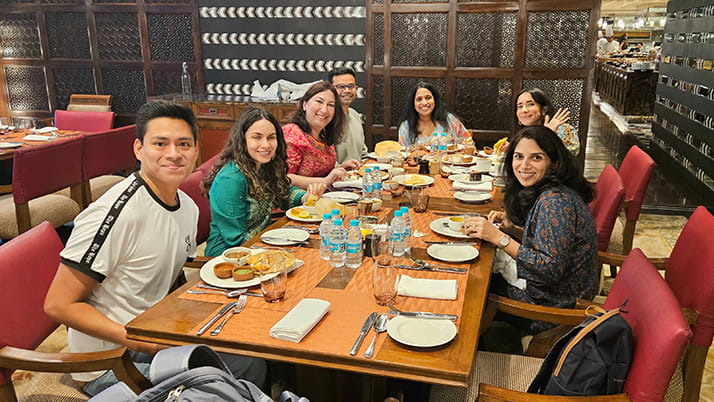 Kellogg students bond over a traditional meal during their TechVenture India course. They sit at a long table at a restaurant, sharing platters of food.