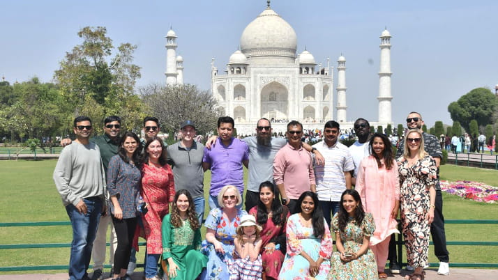 Executive MBA students in the TechVenture India course trip pose for a photograph in front of the Taj Mahal in Agra, India. The iconic white marble mausoleum with its distinctive dome and minarets forms a stunning backdrop against a clear blue sky. 