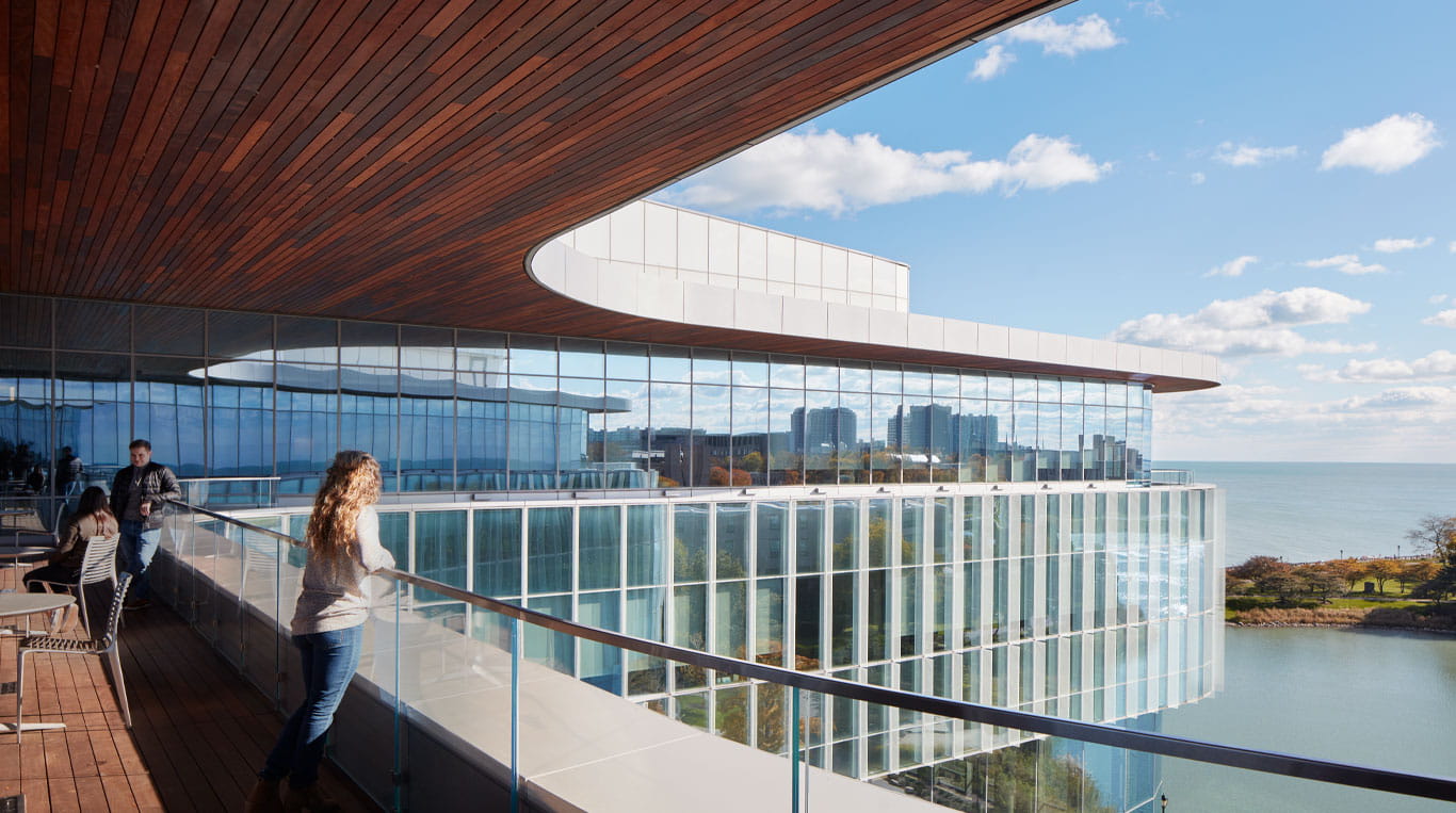 A woman leaning against a balcony railing looking out toward a lake